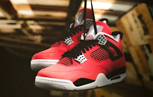 Side view of Air Jordan 4 Retro 'Toro Bravo' basketball sneaker in Fire Red nubuk leather with black wing details, mesh panels, Cement Grey midsole and Jumpman logo