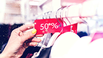 A hand with yellow painted nails holding a clothing tag that says 50% off