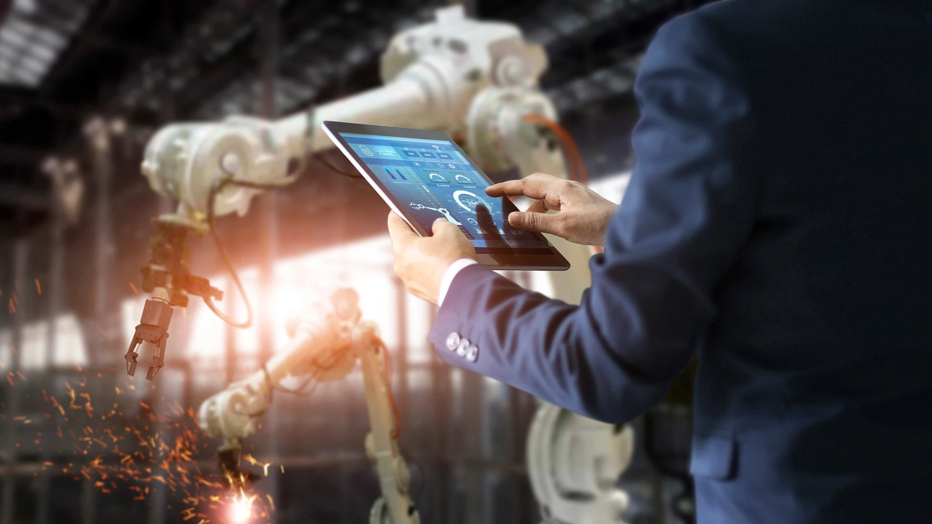Una persona en una tableta trabajando en una fábrica inteligente con brazos robóticos.