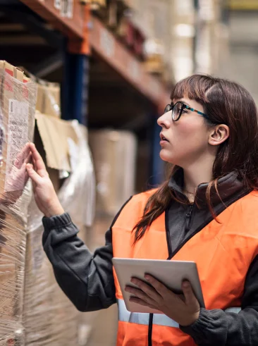 Woman in orange vest counting inventory and reporting it on tablet