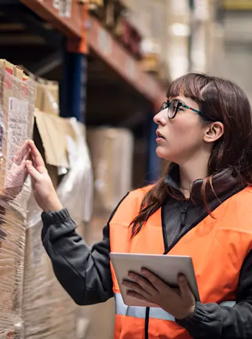 Vrouw in oranje vest telt inventaris en rapporteert het op tablet