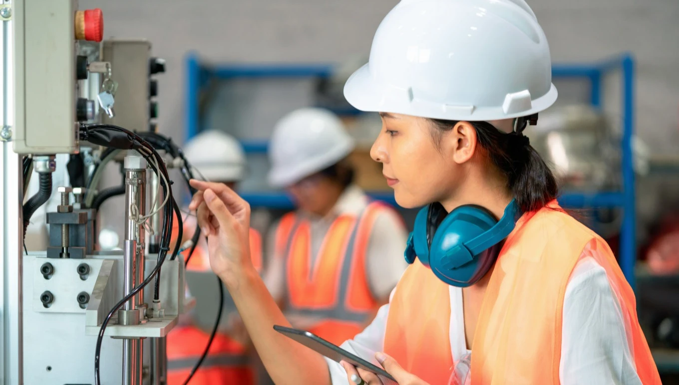 Factory worker inspecting machinery with mobile device in hand