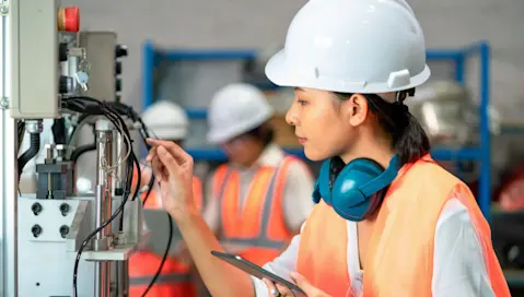 Factory worker inspecting machinery with mobile device in hand