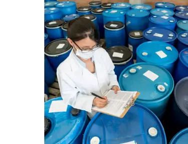 A woman writing on a clipboard surrounded by chemical drums