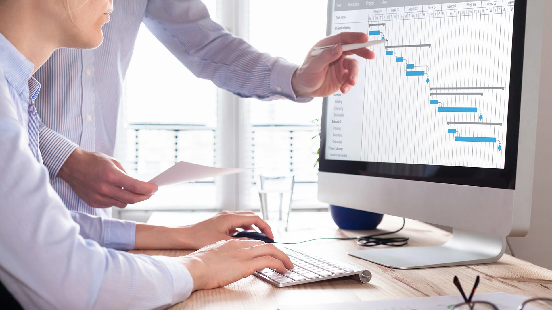 Two people talking business while pointing at charts on a desktop.