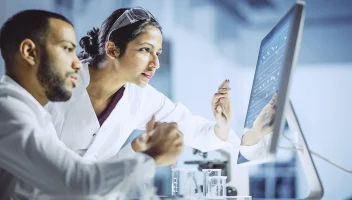 Researchers reviewing report data on monitor screen from lab