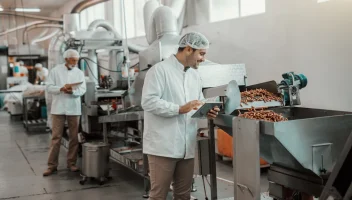 Two food manufacturing workers monitor production lines at a factory.