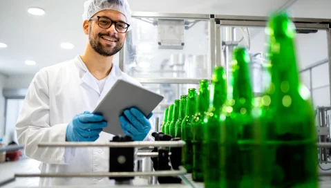 Man in factory checks empty bottles on a conveyor belt.