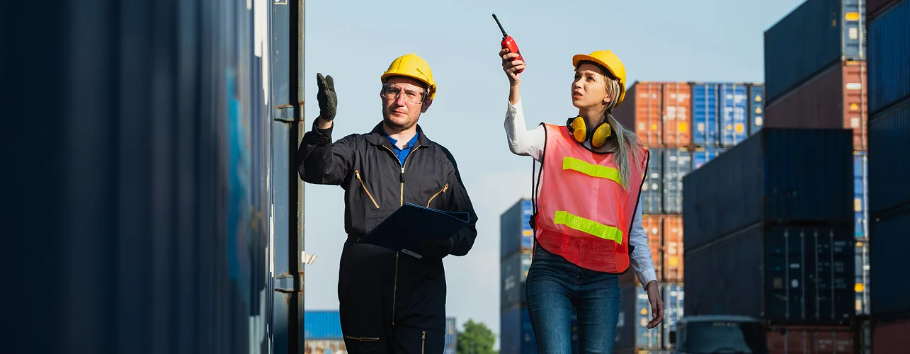 Logistics workers inspecting containers at shipping yard with radio and clipboard