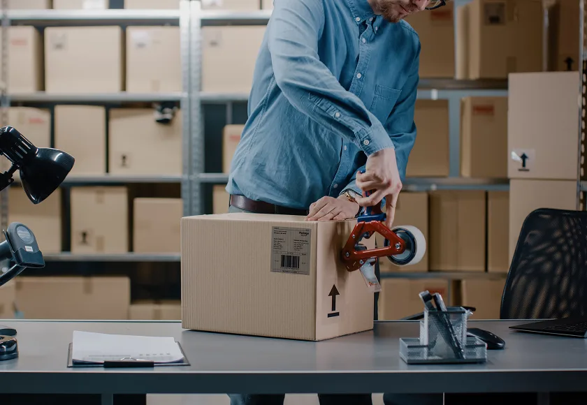 Worker sealing cardboard package at warehouse packing station