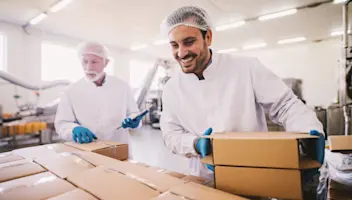 Food facility employees load boxes on a pallet.