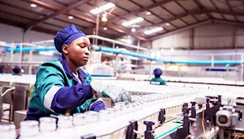 A dairy worker oversees milk bottles moving on a conveyer.