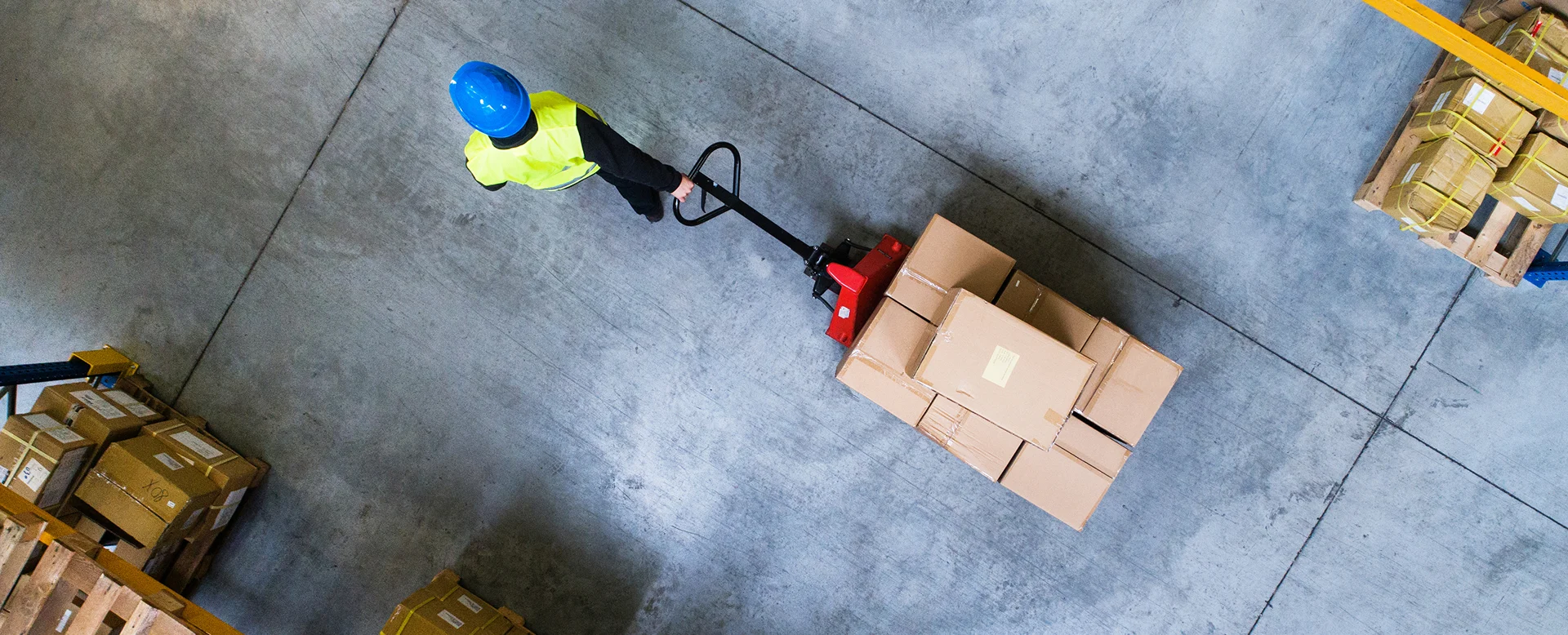 Warehouse worker pulling a pallet truck through a storage facility