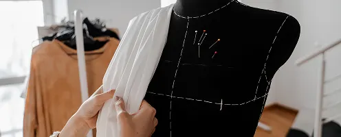 A woman laying fabric over a dress form.
