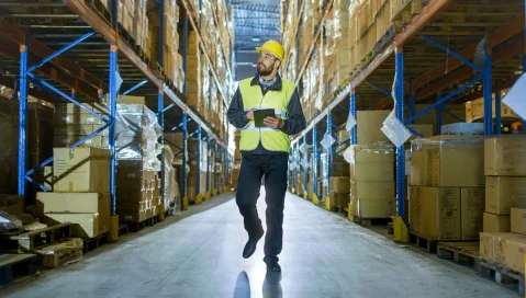 Warehouse worker man reviewing inventory with tablet while walking in warehouse