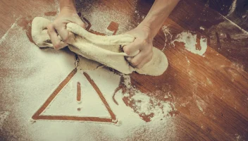 A warning icon has been traced into the flour as a food facility worker kneads dough.