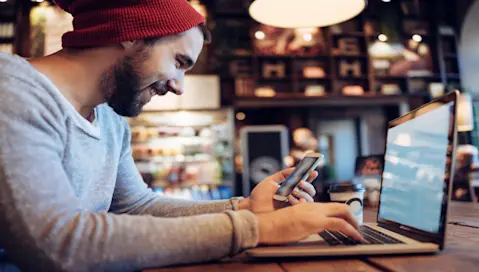 Man using a laptop and phone in a cafe