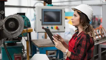 A manufacturing professional in hardhat uses a tablet on the shop floor.