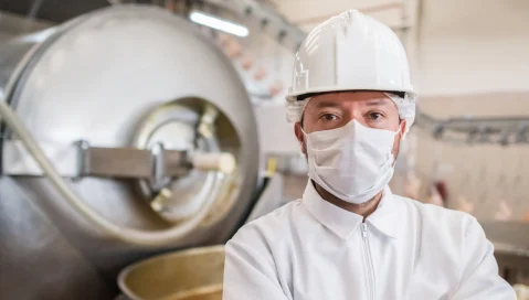 man wearing hardhat and mask in front of a manufacturing equipment