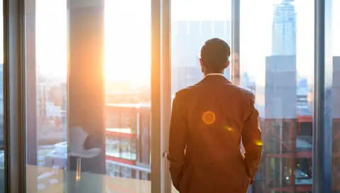 An executive looks out the window in a tall building.