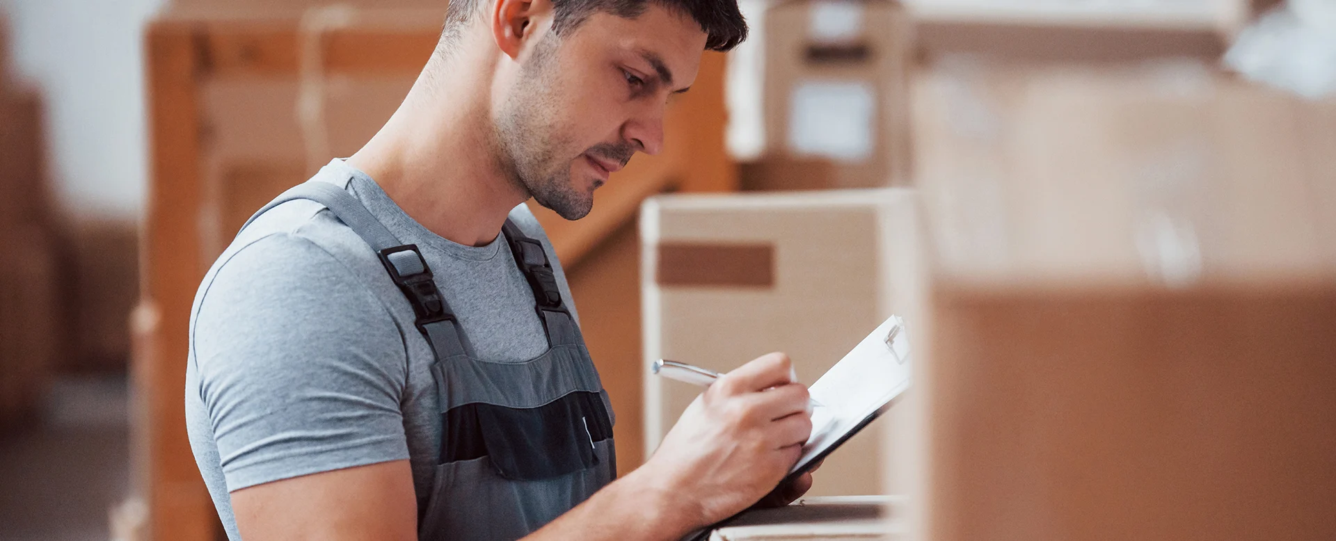 Warehouse worker writing on clipboard while inspecting shipment boxes