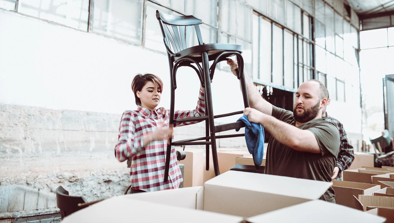 Man and woman loading chair into box for shipping consumer goods retail products.