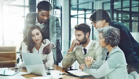 A team of coworkers collaborate during meeting reviewing laptop display.