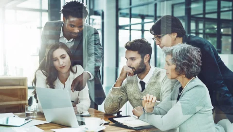 A team of coworkers collaborate during meeting reviewing laptop display.