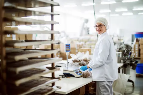 A food facility worker bags cookies at a scale.