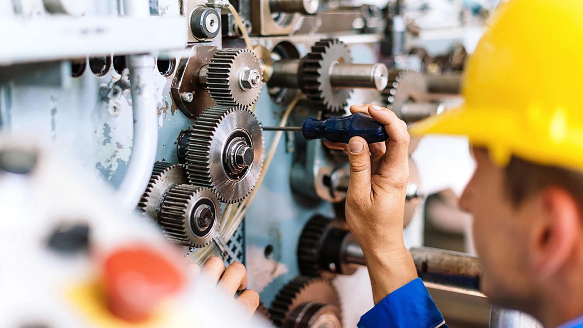Een man met een schroevendraaier werkt aan een machine in een fabriek.