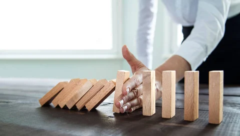 Hand stopping chain of wood blocks falling like dominos