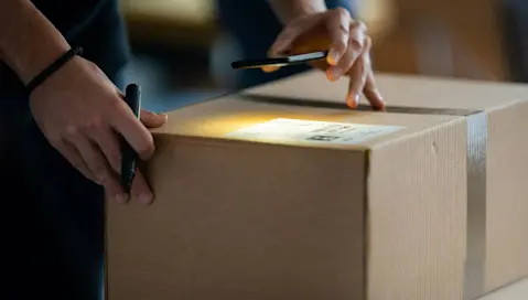 shining light on cardboard box shipping label and marker in hand