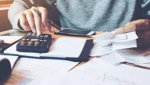 Person with calculator and receipts at desk.