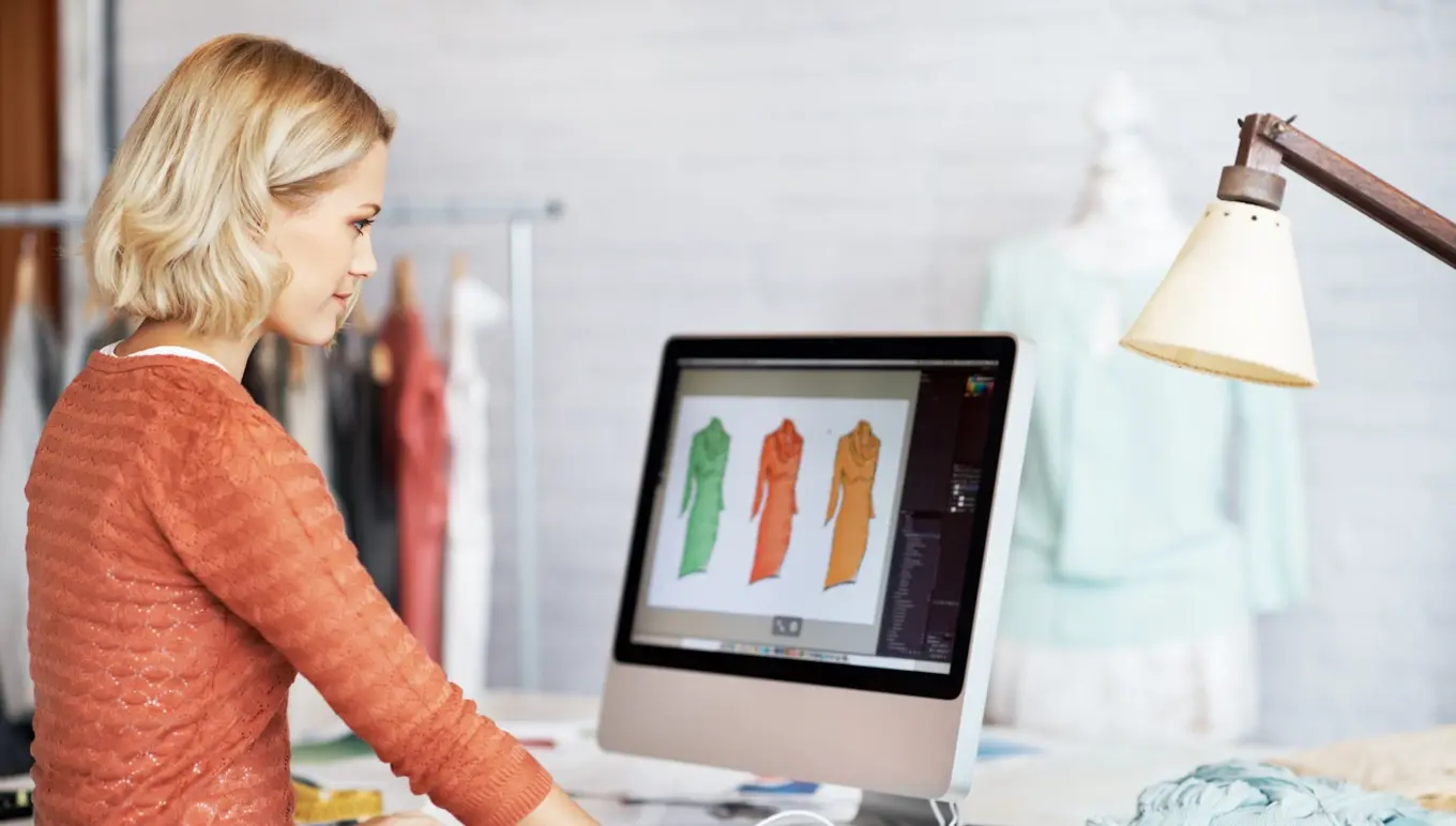 Woman standing at computer looking at clothing sketches.