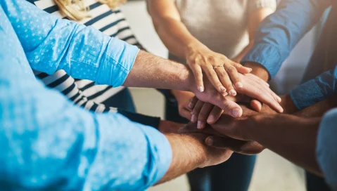 Diverse team members put their hands together in a huddle.