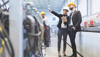 Industrial manufacturing business leaders observe machinery at work.