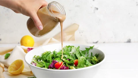 hand pouring dressing on salad