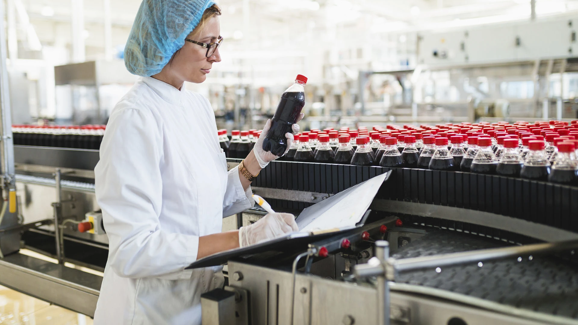 Woman inspecting beverage bottle from assembly line