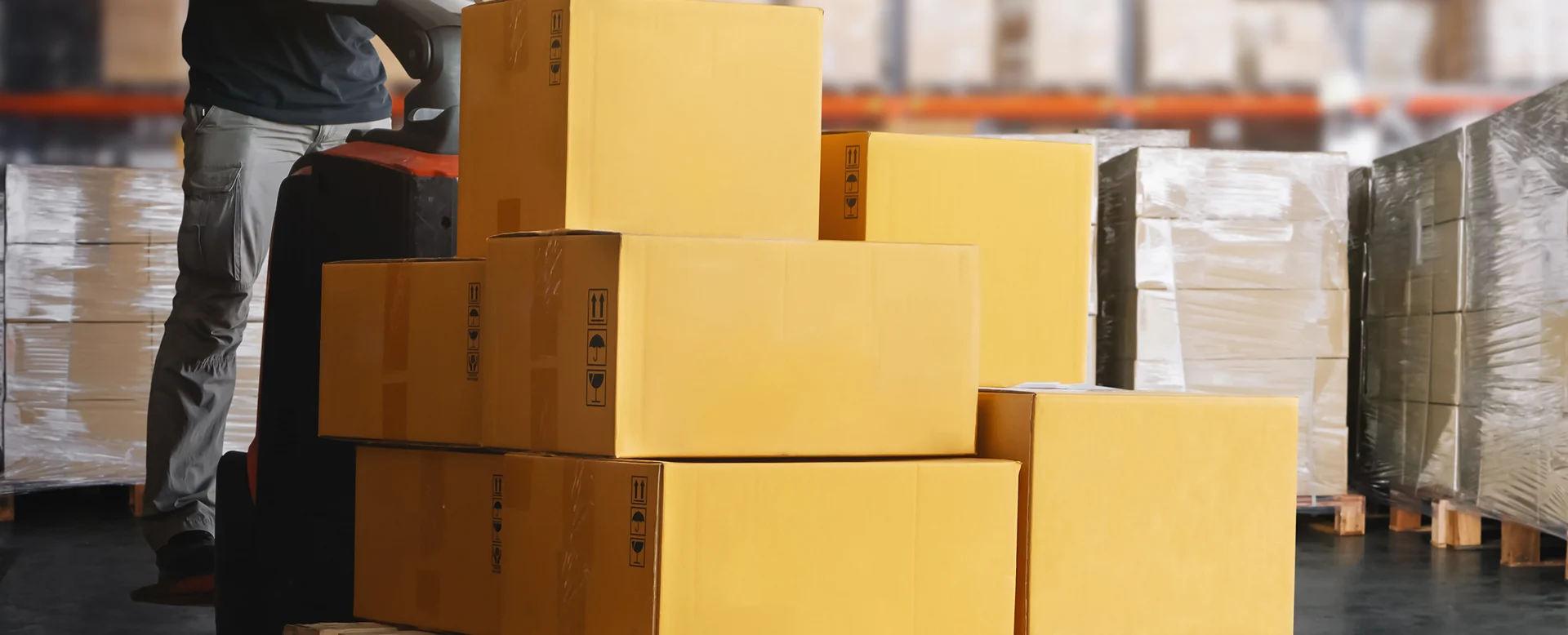 Warehouse worker transporting pallet of boxes with pallet jack