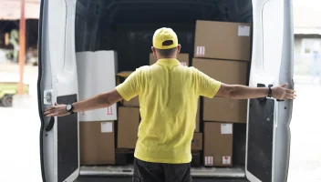 Man in yellow shirt opening delivery van doors and seeing boxes to deliver.