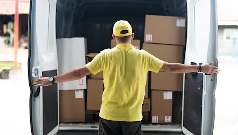 Man in yellow shirt opening delivery van doors and seeing boxes to deliver.