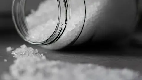 Table salt from a jar is spread across a flat surface.