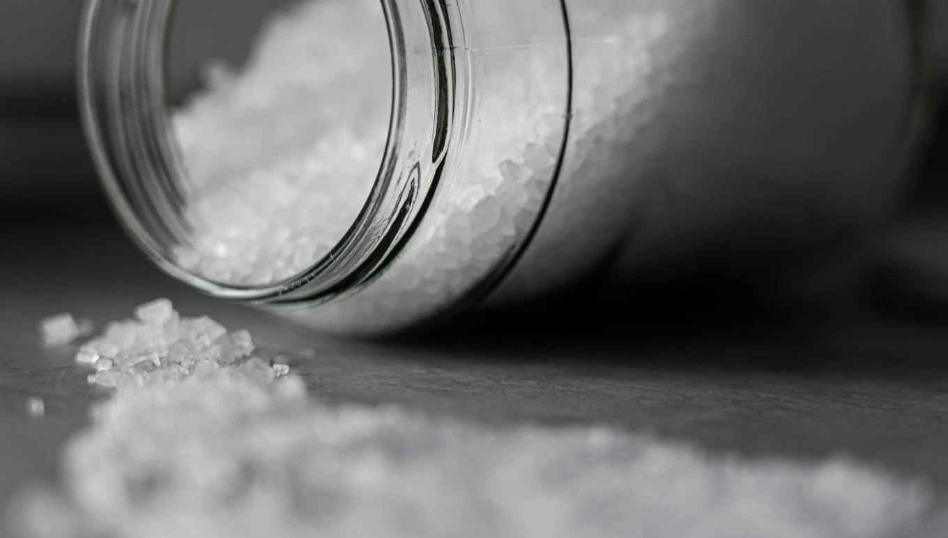 Table salt from a jar is spread across a flat surface.