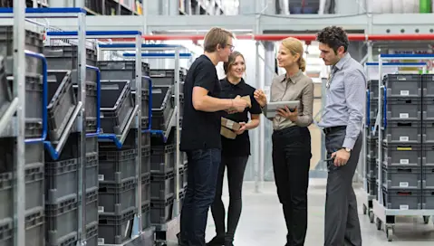 Four people conversing next to stacked plastic crates