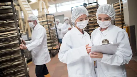 Two food manufacturing facility employees consult a chart.