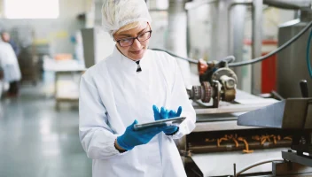 A food facility employee uses a tablet on the factory floor.