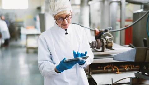 A food facility employee uses a tablet on the factory floor.