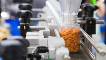 A bottle being filled by pills.