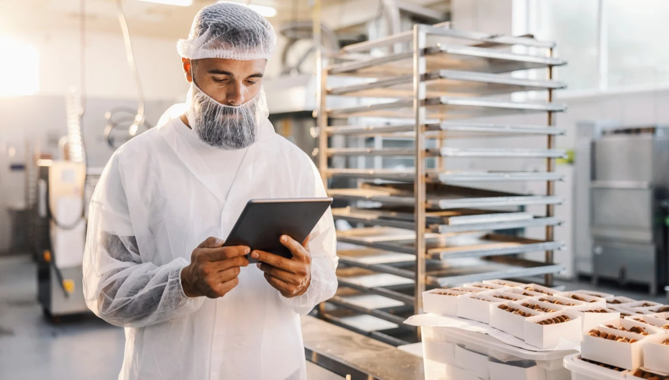 Food factory worker wearing hair and beard net using a touchscreen tablet