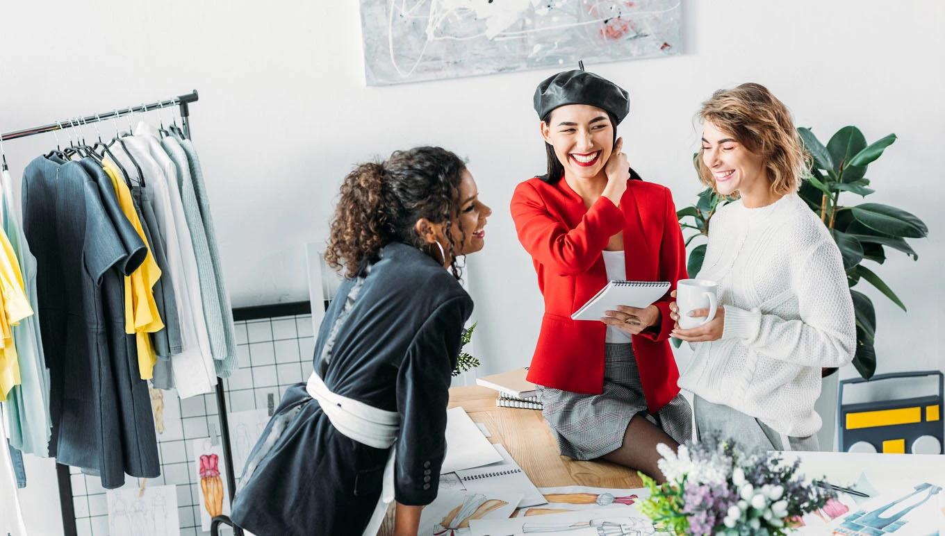Three women fashion designers standing near work desk.